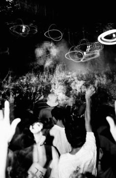 a crowd of people at a concert with their hands in the air and lights above them