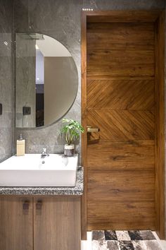 a bathroom sink sitting under a mirror next to a wooden door with a round mirror above it