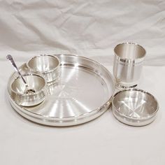 an assortment of silver dishes and cups on a white tableclothed surface with a toothbrush in the middle