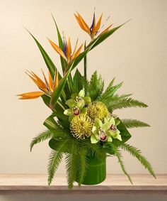 a green vase filled with lots of flowers on top of a wooden table next to a wall