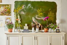 a white cabinet with flowers and plants on it in front of a chalkboard wall