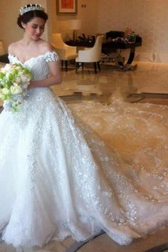 a woman in a white wedding dress holding a bouquet and looking at the camera while wearing a tiara