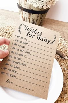 a person is holding up a wish for baby card on a plate next to a flower pot