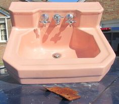 a pink sink sitting on top of a blue table next to a brick building with two faucets