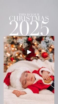 a baby wearing a santa claus outfit laying on top of a bed next to a christmas tree