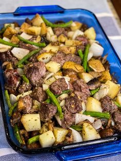 a blue tray filled with meat and vegetables on top of a tablecloth covered table