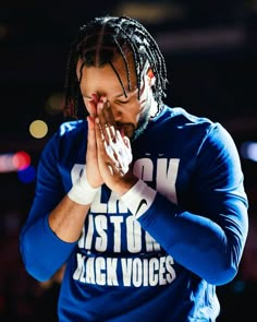 a man with dreadlocks and a blue shirt holding his hands to his face