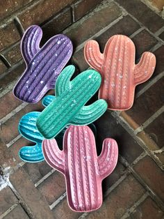 four colorful cactus shaped cookies sitting on top of a brick floor