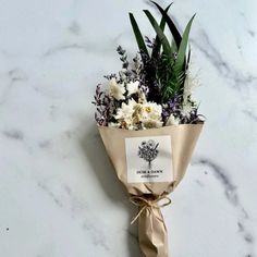 a bouquet of flowers wrapped in brown paper on a marble countertop with the label