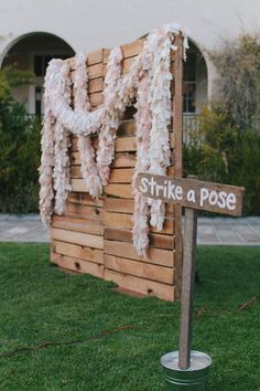 a street sign sitting in the grass next to a wooden structure with flowers on it