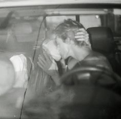 black and white photograph of two people in a car, one kissing the other's head