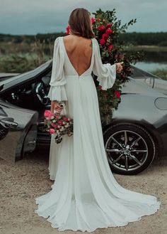 a woman in a white dress standing next to a black car