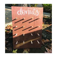 a wooden sign that says donuts on it with pins stuck in the board and some leaves around it