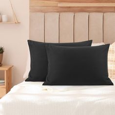 two black pillows sitting on top of a bed next to a night stand and nightstand