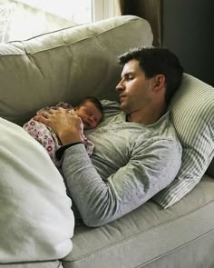 a man laying on top of a couch holding a baby