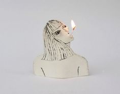 a white ceramic figurine with a lit candle sticking out of it's head