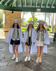 three girls in graduation gowns and caps are standing under a covered area with trees