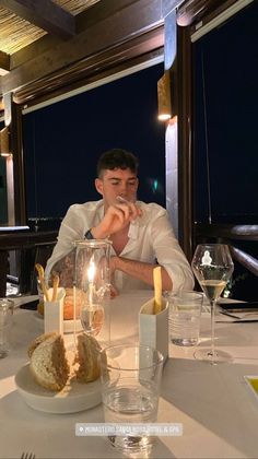 a man sitting at a table with food in front of him and wine glasses on the table