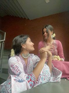 two women sitting next to each other in front of a window with their hands together