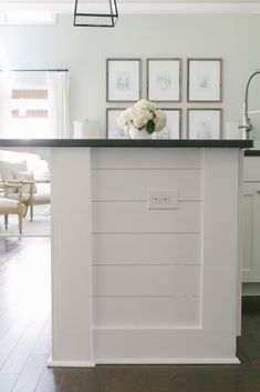 a white kitchen island with black counter top and pictures on the wall above it in a living room