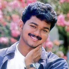 a man with a moustache is posing for a photo in front of pink flowers