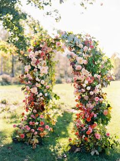 an arch covered in flowers sitting on top of a lush green field