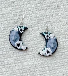 a pair of earrings with flowers on them sitting on top of a white cloth surface