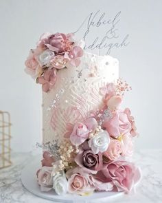 a white and pink wedding cake with flowers on the top is sitting on a table