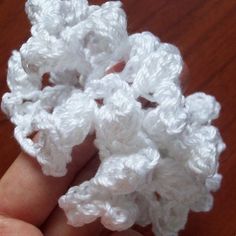 crocheted white flower in hand on wooden table