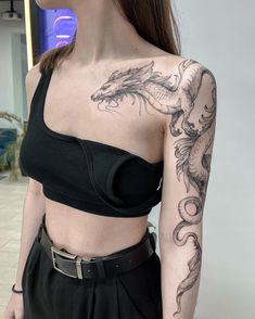 a woman with a dragon tattoo on her arm and shoulder, standing in front of a wall