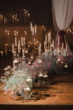 many candles are lit in glass vases on a table