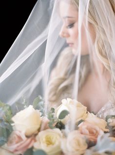 a beautiful blonde woman wearing a wedding veil and holding a bouquet of flowers in front of her face