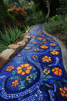 a pathway made out of blue and orange tiles with flowers on the side, surrounded by greenery