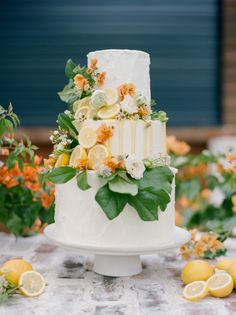 a wedding cake with lemons and greenery on the top is surrounded by flowers