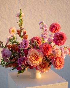 a vase filled with lots of pink and orange flowers on top of a white block