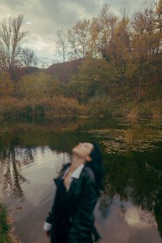 a woman standing in front of a body of water with her eyes closed, looking up at the sky