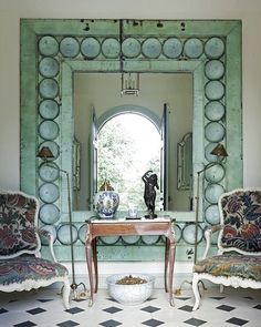 two chairs and a table in front of a mirror with a vase on top of it