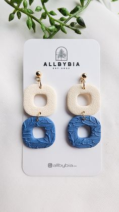 a pair of blue and white earrings sitting on top of a card next to a plant