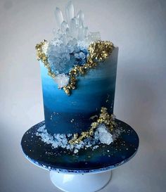 there is a blue and gold cake on top of a white stand with ice crystals