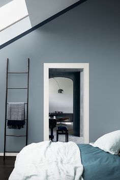 a bedroom with blue walls and white bedding in an atticed space that has a skylight above the bed