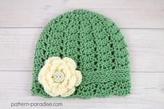 a green crocheted hat with a flower on the front and white flowers on the back