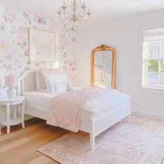 a white bed sitting in a bedroom next to a window with a chandelier