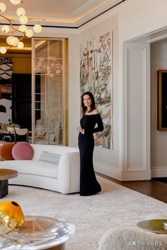 a woman standing in a living room next to a white couch and table with fruit on it