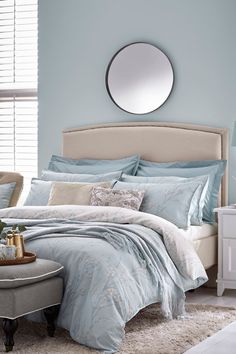 a bed with blue sheets and pillows in front of a round mirror on the wall