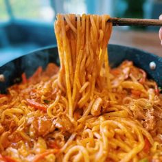 someone is holding chopsticks over noodles in a skillet with meat and vegetables