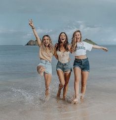 three young women are running in the water at the beach and one is holding her arms up