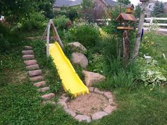 a yellow slide sitting in the middle of a yard next to some rocks and grass