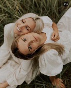 two women laying on the ground in white dresses smiling at the camera with their eyes closed