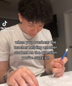 a man sitting at a table writing on paper with a pen in his hand and the caption reads, when you overheat the teacher helping another student on the question you're stuck on