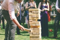 a man is playing with wooden blocks in the grass while other people watch from behind him